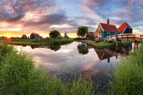 Coucher de soleil sur un canal bordé de roseaux, avec des moulins et des maisons traditionnelles, un aperçu des plus belles villes des Pays-Bas.