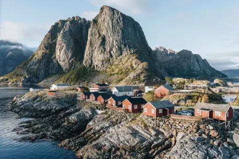 Village de pêcheurs aux maisons rouges sur pilotis, dominant la mer, avec une montagne imposante en arrière-plan. Idéal pour un circuit Lofoten 6 jours.