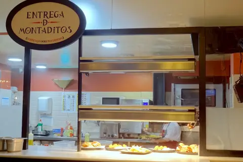 Un comptoir de restaurant à Madrid, avec un panneau "Entrega de Montaditos". Des plats appétissants sont exposés, parfaits pour savoir où manger à Madrid.