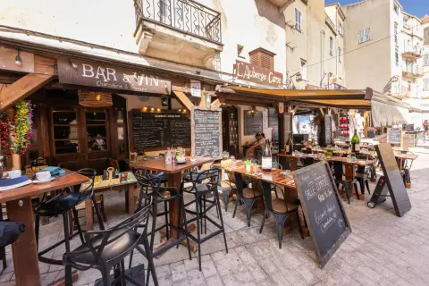 Terrasse d'un restaurant "Bar à Vin" dans le restaurant bonifacio vieille ville. Tables dressées, chaises noires, ardoises de menu. Ambiance estivale.