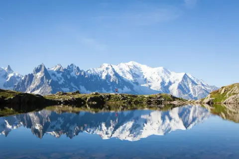 Un randonneur en rouge célèbre la beauté de cet endroit paradisiaque en France, avec le Mont Blanc majestueux se reflétant dans un lac alpin paisible.