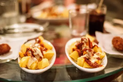 Patatas bravas, un classique pour savoir où manger à Barcelone. Des tapas savoureuses sur une table en verre.