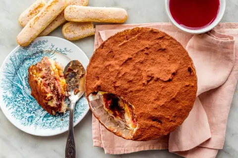 Délicieuse zuppa inglese recette, avec une part déjà servie sur une assiette ornée. Des biscuits à la cuillère et une coupelle de coulis complètent ce dessert gourmand.