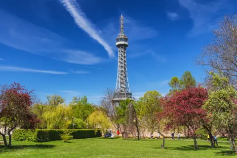 La tour Eiffel de Prague, une structure métallique imposante, se dresse fièrement au milieu d'un parc verdoyant et fleuri sous un ciel bleu éclatant.