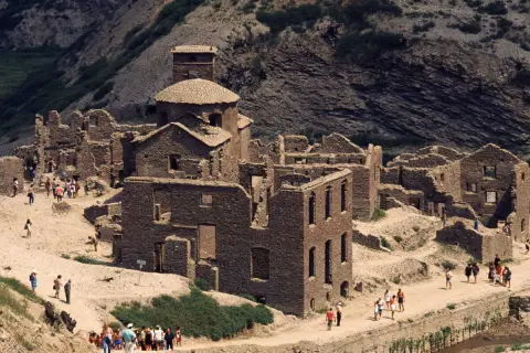Ruines de pierre du lago di vagli, un village fantôme envahi par la végétation, avec des visiteurs explorant les vestiges.