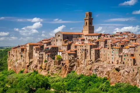 Vue panoramique de Magliano in Toscana, un village médiéval perché sur une falaise, avec ses maisons en pierre et son clocher imposant sous un ciel bleu.