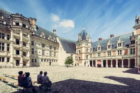 Cour intérieure du château de Blois, avec des visiteurs profitant du temps de visite. Architecture Renaissance sous un ciel bleu.