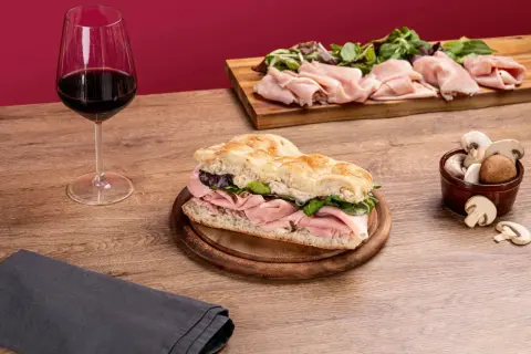 Une délicieuse schiacciata garnie de jambon et de verdure, accompagnée d'un verre de vin rouge et de champignons frais.