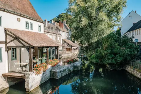 Maison ancienne au bord d'une rivière, idéale pour visiter Chartres à pied. Fleurs rouges et reflets dans l'eau.