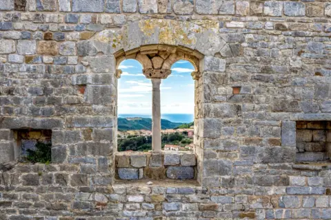 Fenêtre médiévale à Campiglia Marittima offrant une vue sur la mer et les toits du village.