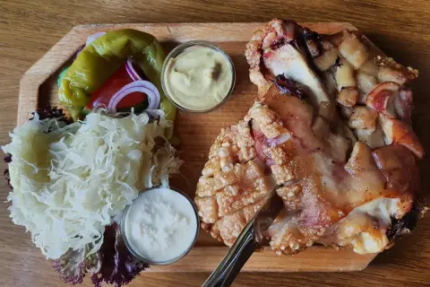 Un plat tcheque copieux : un jarret de porc rôti à la peau croustillante, servi avec de la choucroute, des poivrons, des oignons rouges et deux sauces.