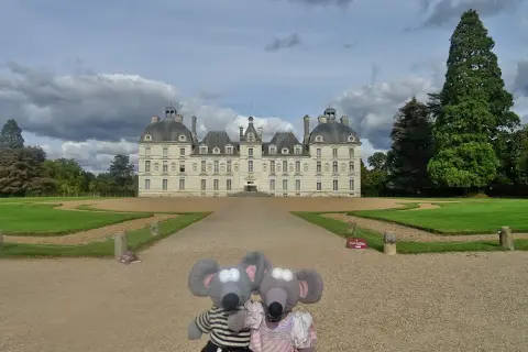 Deux souris en peluche devant le majestueux château de Cheverny, un jour de ciel nuageux.
