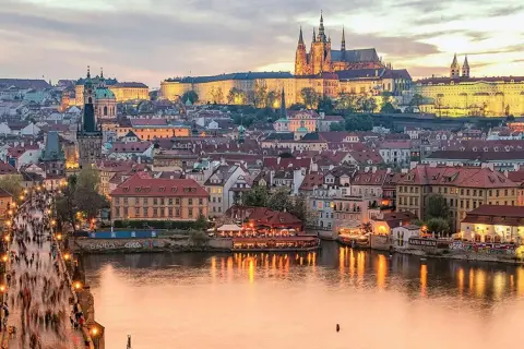 Prague en ce moment : le pont Charles animé, le château illuminé et la Vltava reflétant les lumières de la ville.