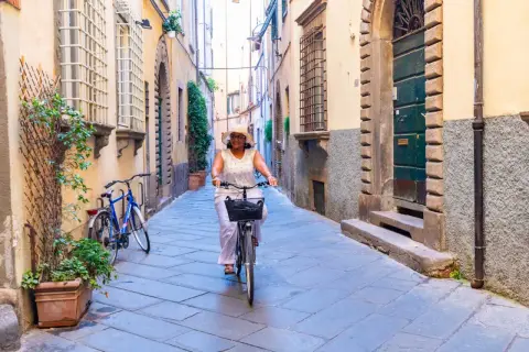 Une femme souriante fait du vélo dans une ruelle pavée, profitant d'une belle journée à Florence.