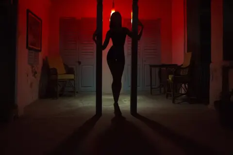 Silhouette d'une femme dans un décor rouge, évoquant l'ambiance du quartier rouge de Prague. Des chaises et des portes bleues créent un contraste saisissant.