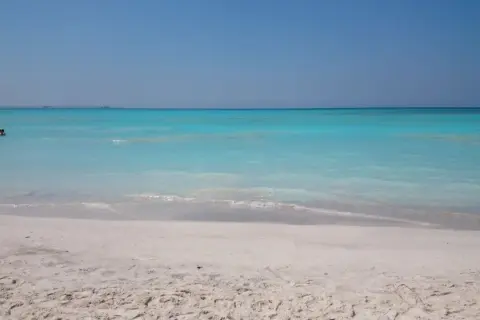 Plage de Rosignano Marittimo, mer turquoise et sable blanc. Deux personnes nagent paisiblement dans l'eau claire.