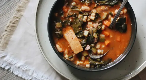 Un bol de ribollita toscana, une soupe épaisse et réconfortante avec des légumes verts, des haricots et des pâtes, servie avec une cuillère.