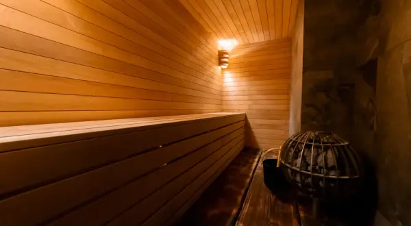 Intérieur d'une **sauna Prague** chaleureuse, avec des bancs en bois clair, un poêle à pierres et un éclairage doux.