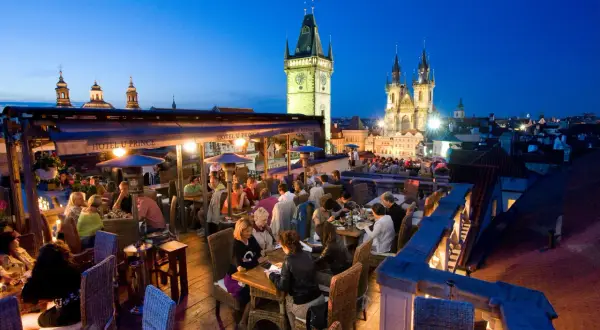 Dîner sur un rooftop à Prague, avec vue sur la tour de l'horloge et l'église Notre-Dame du Týn. Ambiance chaleureuse.