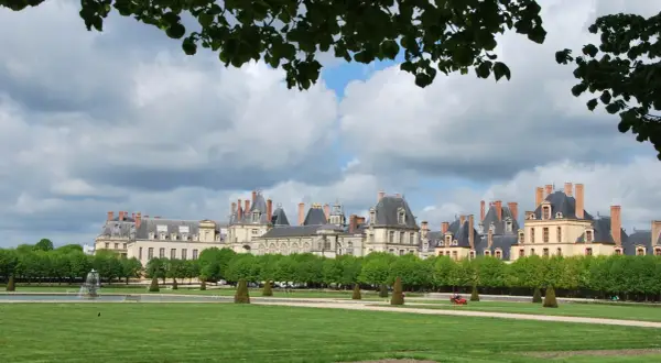 Magnifique vue du château de Fontainebleau, idéal pour visiter. Pelouse verdoyante, fontaine et arbres taillés.
