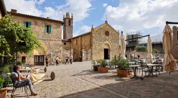 Place pavée de Monteriggioni, Italie, avec une église médiévale et des tables de café.
