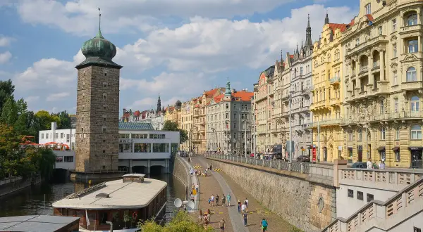 Vue animée de la Vltava, idéale pour visiter Prague en 1 jour. La tour de la Poudrière et les façades colorées des immeubles bordent la promenade.