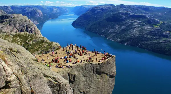 Vue spectaculaire sur un fjord norvégien, avec des randonneurs profitant du paysage. Un souvenir parfait de notre road trip Scandinavie 2 semaines.