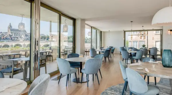 Salle lumineuse avec vue panoramique sur la Loire. Tables dressées, chaises bleues confortables. Un cadre idéal pour découvrir les restaurants de la Loire.