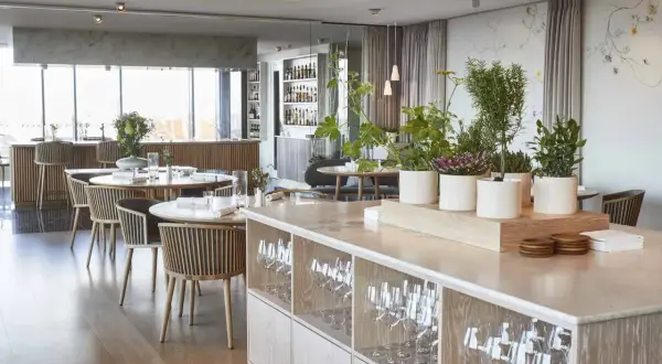 Ambiance élégante d'un restaurant à Copenhague, avec des tables dressées, des plantes et une vue sur le bar. Idéal pour découvrir les meilleurs restaurants Copenhague.