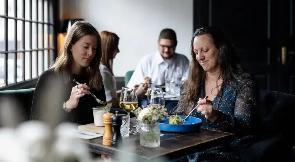Ambiance chaleureuse pour savoir où manger à Honfleur. Quatre personnes savourent un repas dans un restaurant cosy.
