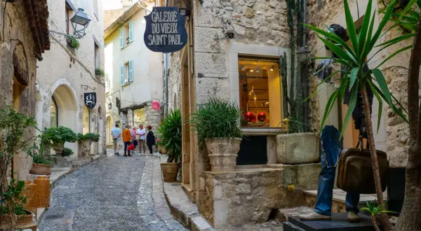 Ruelle pavée à Saint-Paul-de-Vence, avec des boutiques, des plantes et des touristes.