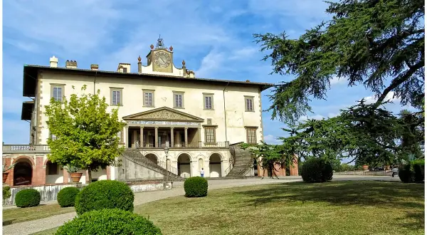 La villa Poggio a Caiano, un joyau architectural, se dresse sous un ciel bleu. Des arbres majestueux ombragent la pelouse verdoyante et les buissons taillés.