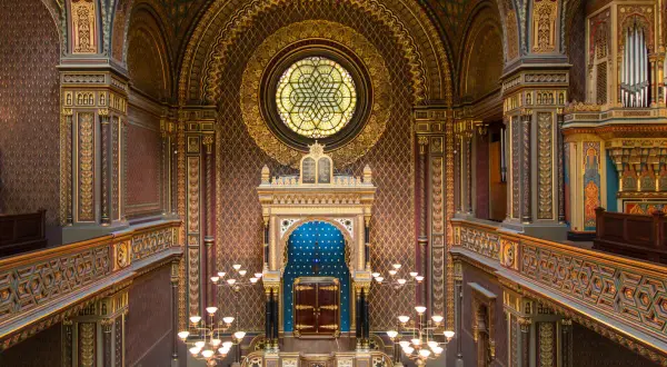 Intérieur orné de la synagogue espagnole de Prague, avec un vitrail circulaire, un Aron Kodesh bleu et des lustres dorés.