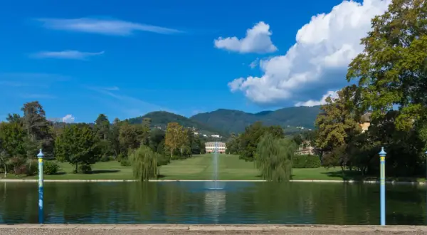 Le parc de la villa reale di Marlia s'étend devant un étang paisible, avec une fontaine jaillissant au centre. Des arbres majestueux bordent la pelouse menant à la villa.