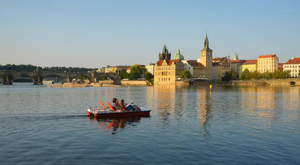 Un couple profite d'une balade en pédalo sur la Vltava, offrant une perspective insolite de Prague et de son pont emblématique au coucher du soleil.