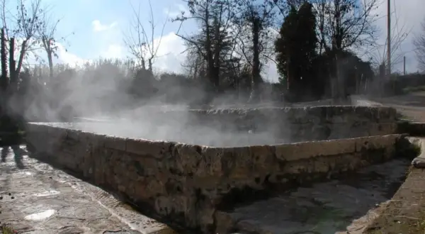 Bains antiques en pierre à San Casciano dei Bagni, dégageant une vapeur d'eau chaude sous un ciel bleu.