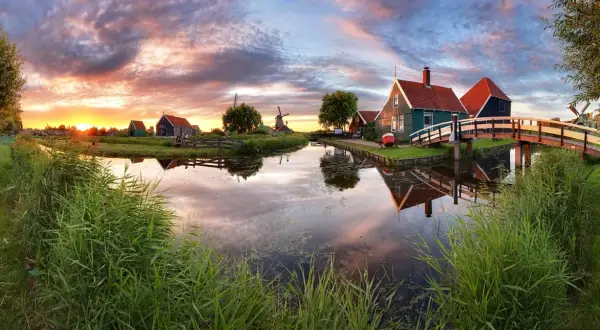 Coucher de soleil sur un canal bordé de roseaux, avec des moulins et des maisons traditionnelles, un aperçu des plus belles villes des Pays-Bas.