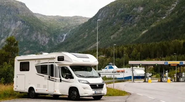 Camping-car blanc prêt pour un road trip en Norvège en camping-car budget, avec un ferry et des montagnes en arrière-plan.