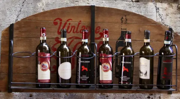 Huit bouteilles de vin, dont plusieurs de **vin de Toscane**, alignées sur une étagère en bois ornée d'une inscription "Vintage".