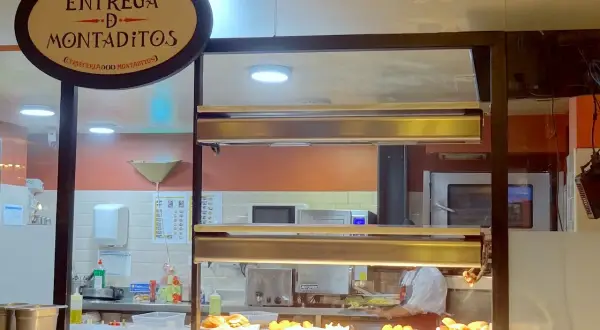 Un comptoir de restaurant à Madrid, avec un panneau "Entrega de Montaditos". Des plats appétissants sont exposés, parfaits pour savoir où manger à Madrid.