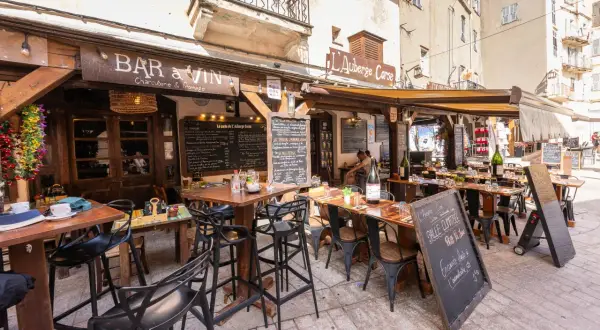 Terrasse d'un restaurant "Bar à Vin" dans le restaurant bonifacio vieille ville. Tables dressées, chaises noires, ardoises de menu. Ambiance estivale.