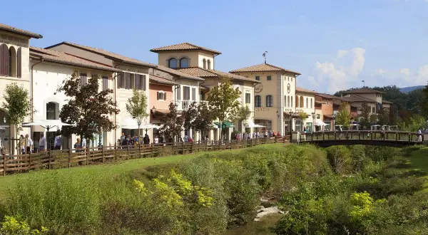 Boutiques colorées le long d'une rivière à Barberino di Mugello, avec des passants sur un pont en bois.
