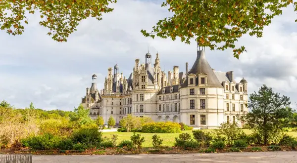 Magnifique château avec ses nombreuses tours et tourelles, entouré d'arbres aux couleurs d'automne. Un paysage de rêve.