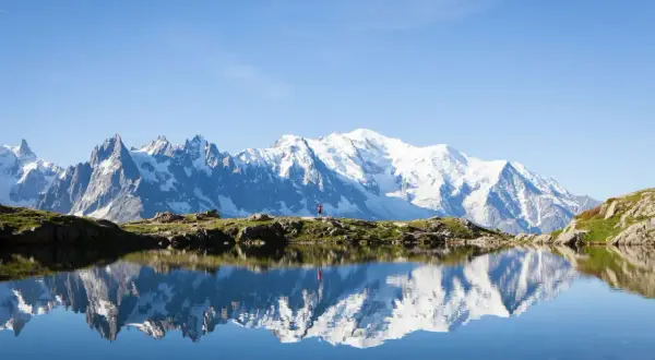 Un randonneur en rouge célèbre la beauté de cet endroit paradisiaque en France, avec le Mont Blanc majestueux se reflétant dans un lac alpin paisible.