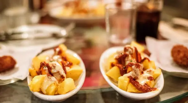 Patatas bravas, un classique pour savoir où manger à Barcelone. Des tapas savoureuses sur une table en verre.