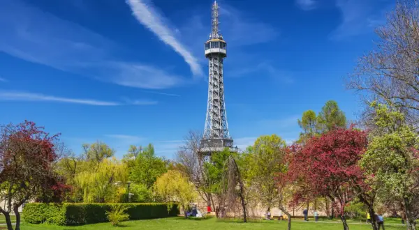 La tour Eiffel de Prague, une structure métallique imposante, se dresse fièrement au milieu d'un parc verdoyant et fleuri sous un ciel bleu éclatant.