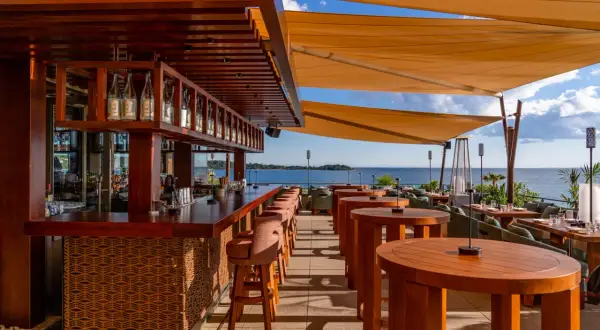 Bar de plage à Cannes avec vue sur la mer. Tables en bois, tabourets de bar et voiles d'ombrage.
