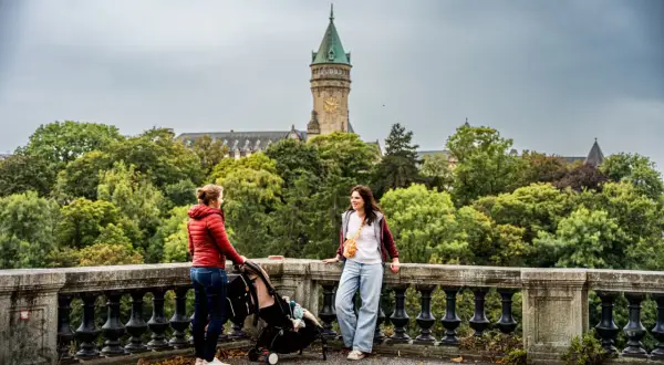 Deux femmes discutent près d'une poussette, avec une vue sur le Palais de la Banque d'État. Un aperçu de ce que l'on peut voir en visiter le Luxembourg en 3 jours.