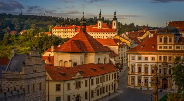 Vue panoramique de Prague au coucher du soleil, avec les toits rouges et les tours du monastère de Strahov dominant le paysage.