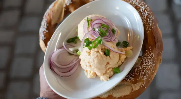 Un plat de fromage à tartiner avec des oignons rouges et de la ciboule, servi avec un bretzel salé, parfait pour un beer garden.